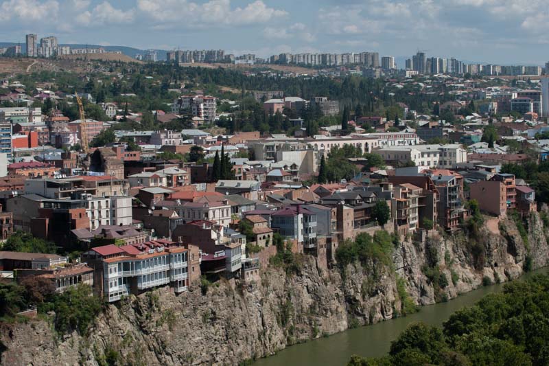 Tiflis - Im Vordergrund der Fluss Mtkwari, dahinter einige Jahundertwendegebäude und die Wohnsiedlungen der Vorstadt.